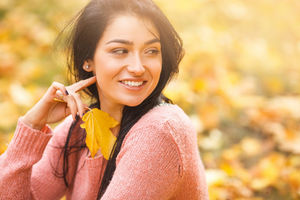 Woman holding a fall leaf looking over her shoulder.