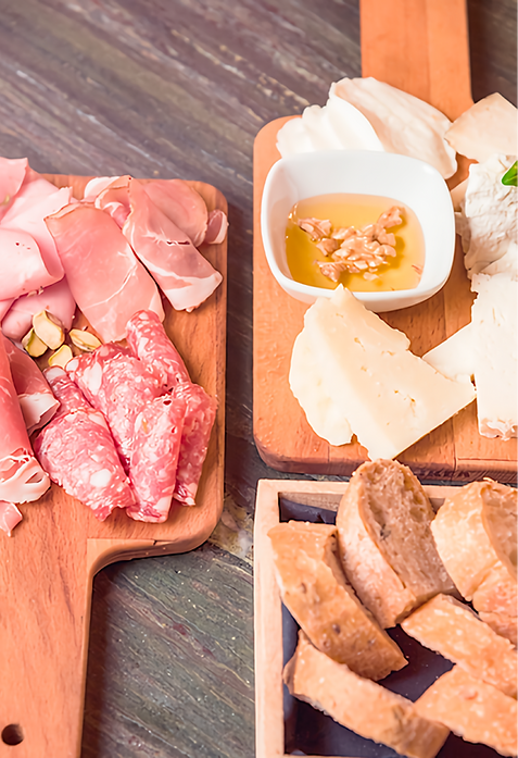 wooden boards with salami, jamon, and cheese, a plate of honey and nuts, and a basket of bread