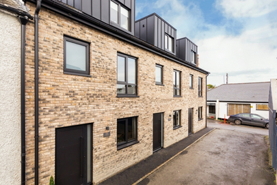 Greenmount Homes, Project by Greenlight, Residential Development – Row of three modern three-storey townhouses with brick facades, black-framed windows, and dormer-style upper floors, situated along a narrow paved lane.