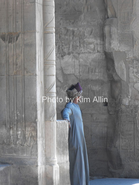 An Egyptian man standing in a temple, wearing traditional robes.