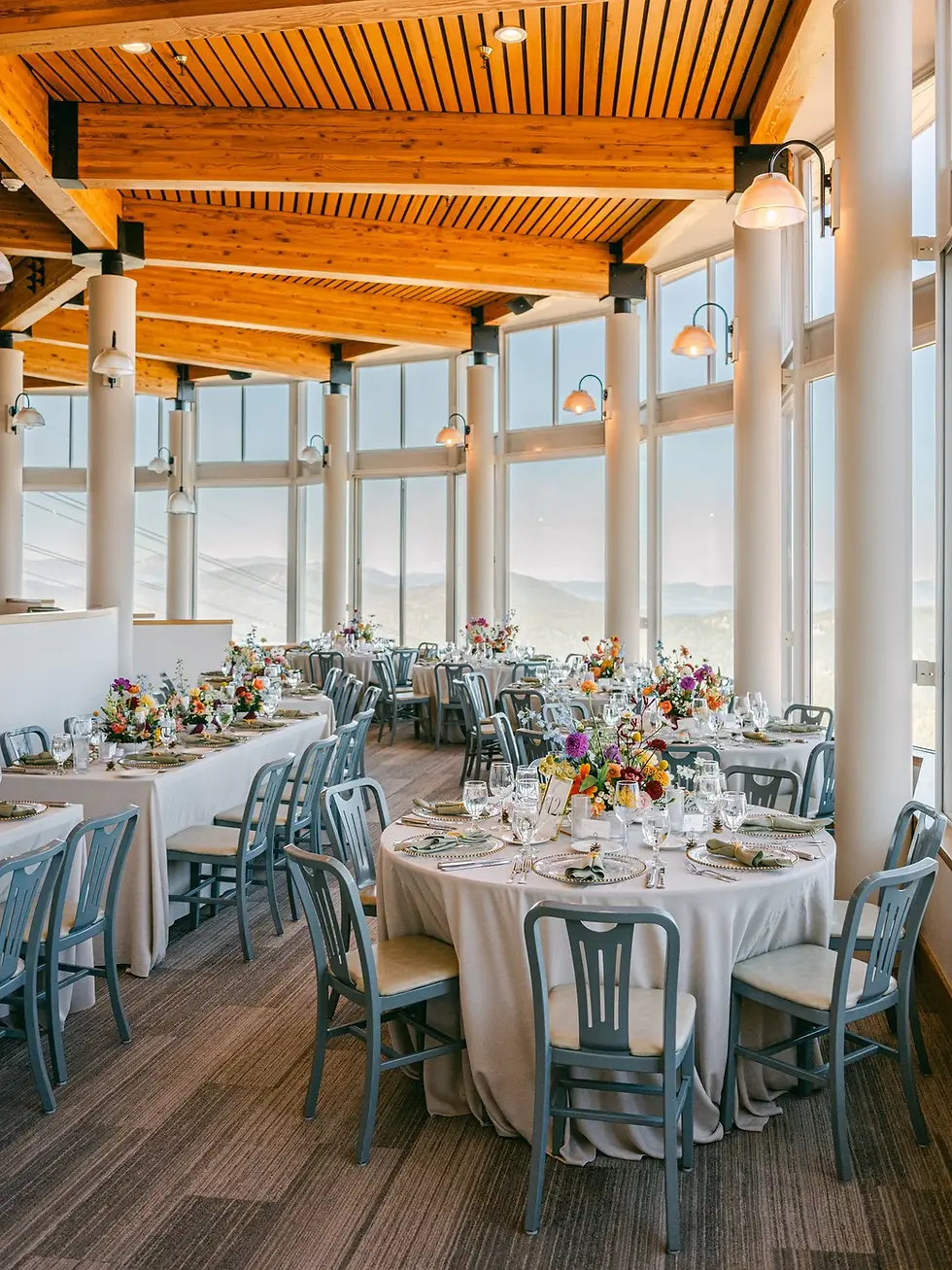Palisades Hight Camp Elegant dining room with round tables, gray chairs, colorful floral arrangements, and large windows. Warm wooden ceiling and bright ambiance.