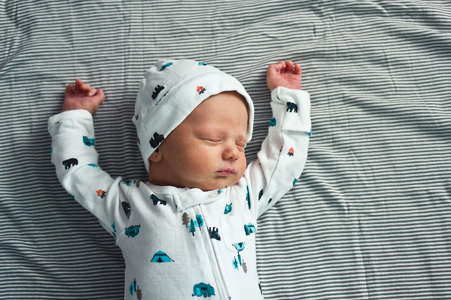 Image of sleeping infant with his hands up and a white bodysuit and matching hat