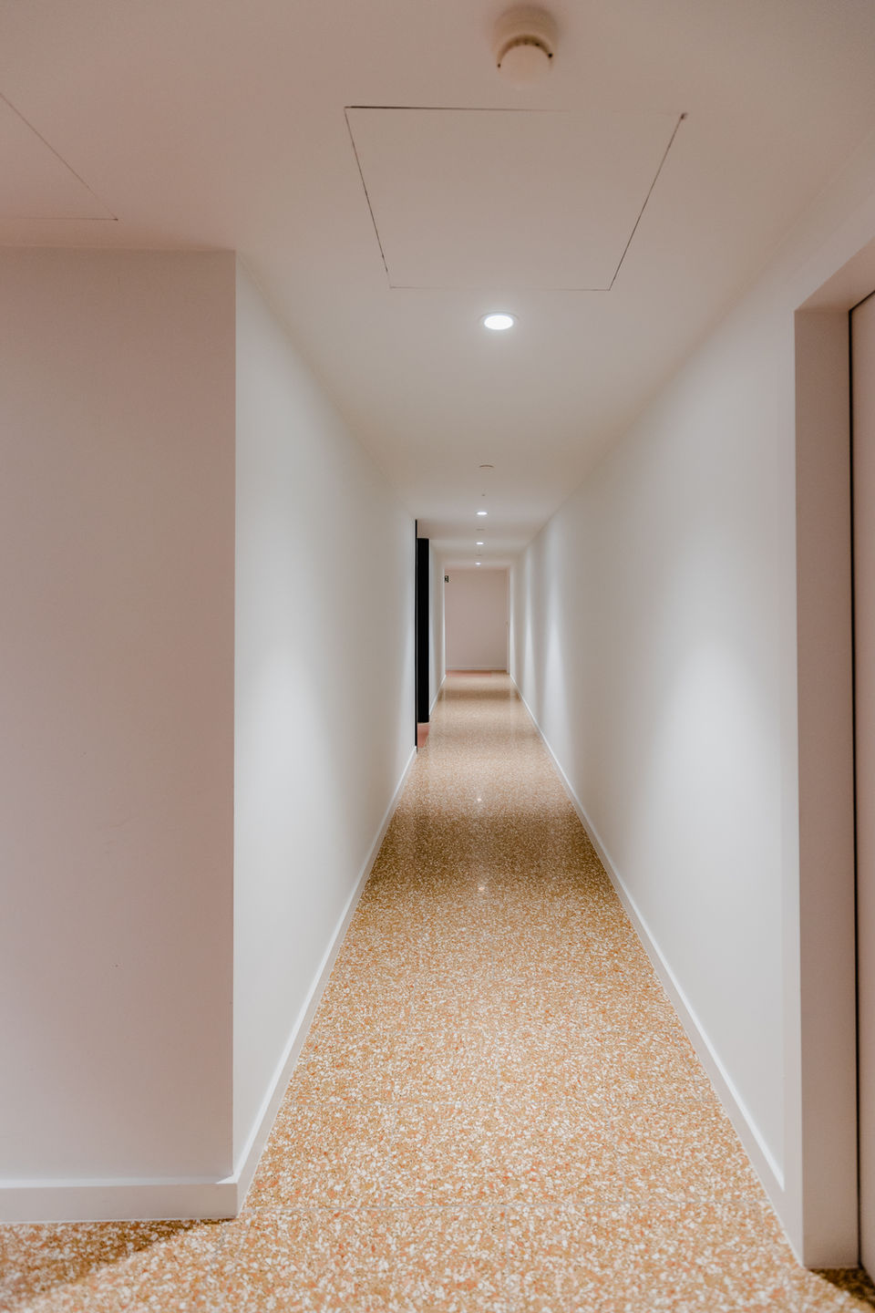 Terrazzo vloertegels geplaatst in halfsteensverband in de gang van een appartementsgebouw.