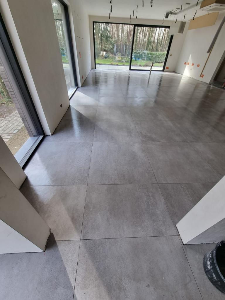 Plaatsing van grote XXL betonlook vloertegels in moderne leefruimte met zicht op tuin, door Cerafloor.