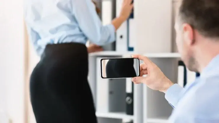 Muž fotiaci si pozadie kolegyne v sukni.