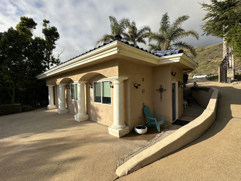 Angled view of a finished Malibu ADU with stucco exterior, arched columns, blue tile roof, exterior lights, and driveway, built by Built to Perfection, Inc.