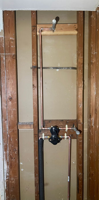 Progress photo of a Newbury Park bathroom remodel showing an open stud wall with new copper shower plumbing, mixing valve, and riser pipe installed before drywall and tile.