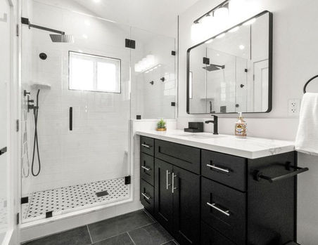 Modern bathroom with a black vanity and quartz countertop, large mirror with vanity lights, and a frameless glass shower with white subway tile and patterned mosaic shower floor.