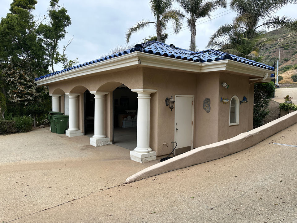 Before photo of an existing Malibu garage with stucco walls, arched columns, blue tile roof, and a sloped driveway prior to ADU construction by Built to Perfection, Inc.