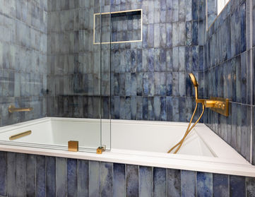 After photo of a bathroom soaking tub with deep blue vertical tile walls, a recessed niche, glass panel, and brushed gold shower fixtures in Norwalk, California.