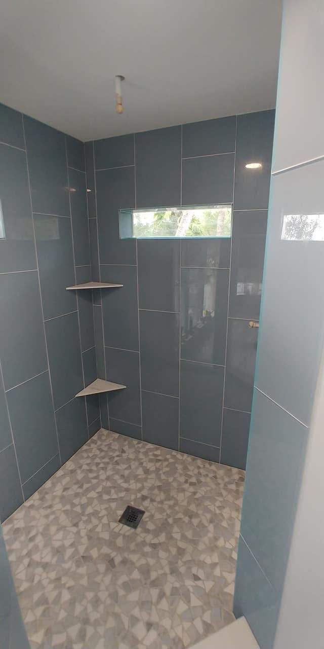 Modern bathroom shower remodel with dark gray wall tiles and corner shelves