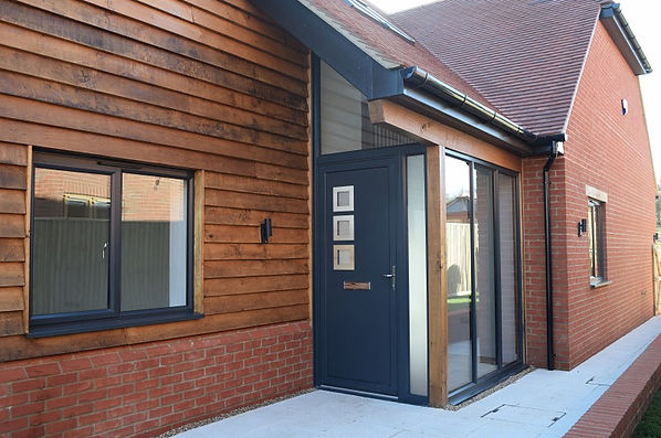 Large anthracite grey aluminium entrance door with full-height glazing installed at a timber-clad home in Harwell