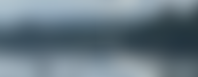 Two sailboats anchored in calm waters near a forested shoreline, with overcast skies and scattered clouds above a distant tree-covered hill.Two sailboats anchored in calm waters near a forested shoreline, with overcast skies and scattered clouds above a distant tree-covered hill.