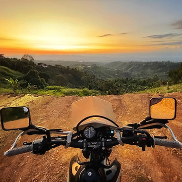 motorbike handlebars on dirt road facing sunset