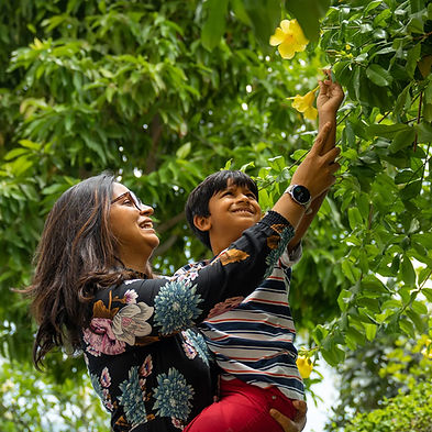 Smilestones Cambodia Founder & CEO and a child reaching for yellow flowers outdoors, illustrating the family and environment coaching provided by Smilestones Cambodia