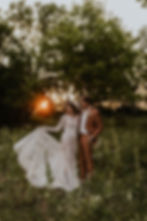 Boho bride and groom kissing at sunset in a field.