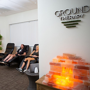 The ground therapy studio is shown with a salt lamp in the foreground. There are two patients using ground therapy recliners to meditate.