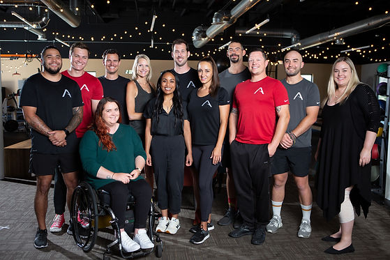 A group photo with 12 men and women who work at Adapt, standing and smiling. One person is a wheelchair user.