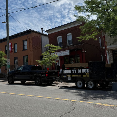 A Mighty Mouse Junk Removal truck is parked on a sunny urban street in Ottawas chinatown. Vibrant green trees and a clear blue sky create a picturesque neighbourhood scene.