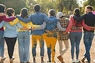 Diverse group of friends hugging outdoors from behind.