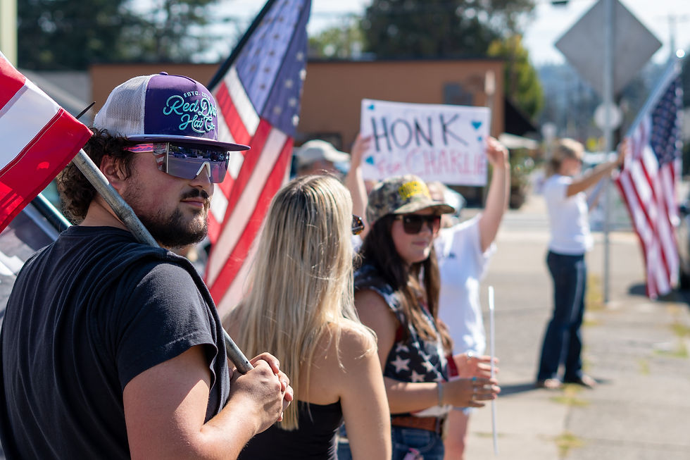 Supporters holding American flags gather along the roadside, eagerly awaiting the memorial ride for Charlie Kirk.