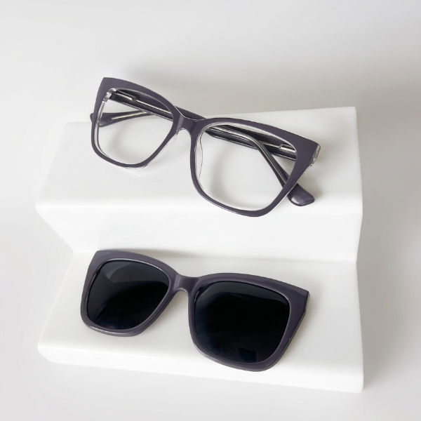 Óculos de grau feminino Samia transparente com lente clip-on solar magnética em suporte branco, estilo editorial.