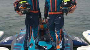 E1 Team Miami racers standing on their electric race boat holding helmets, wearing blue and orange team suits.