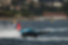 Electric race boat from Team Miami skimming water with red rear fin and coastal city backdrop.