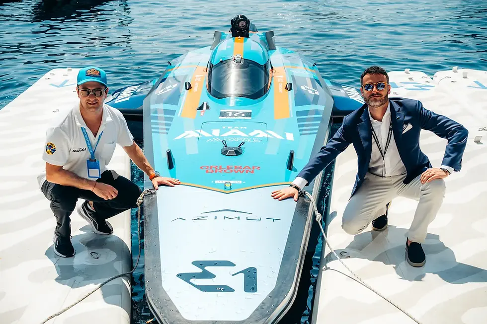 Two Team Miami members pose next to the E1 electric race boat docked in crystal blue water.