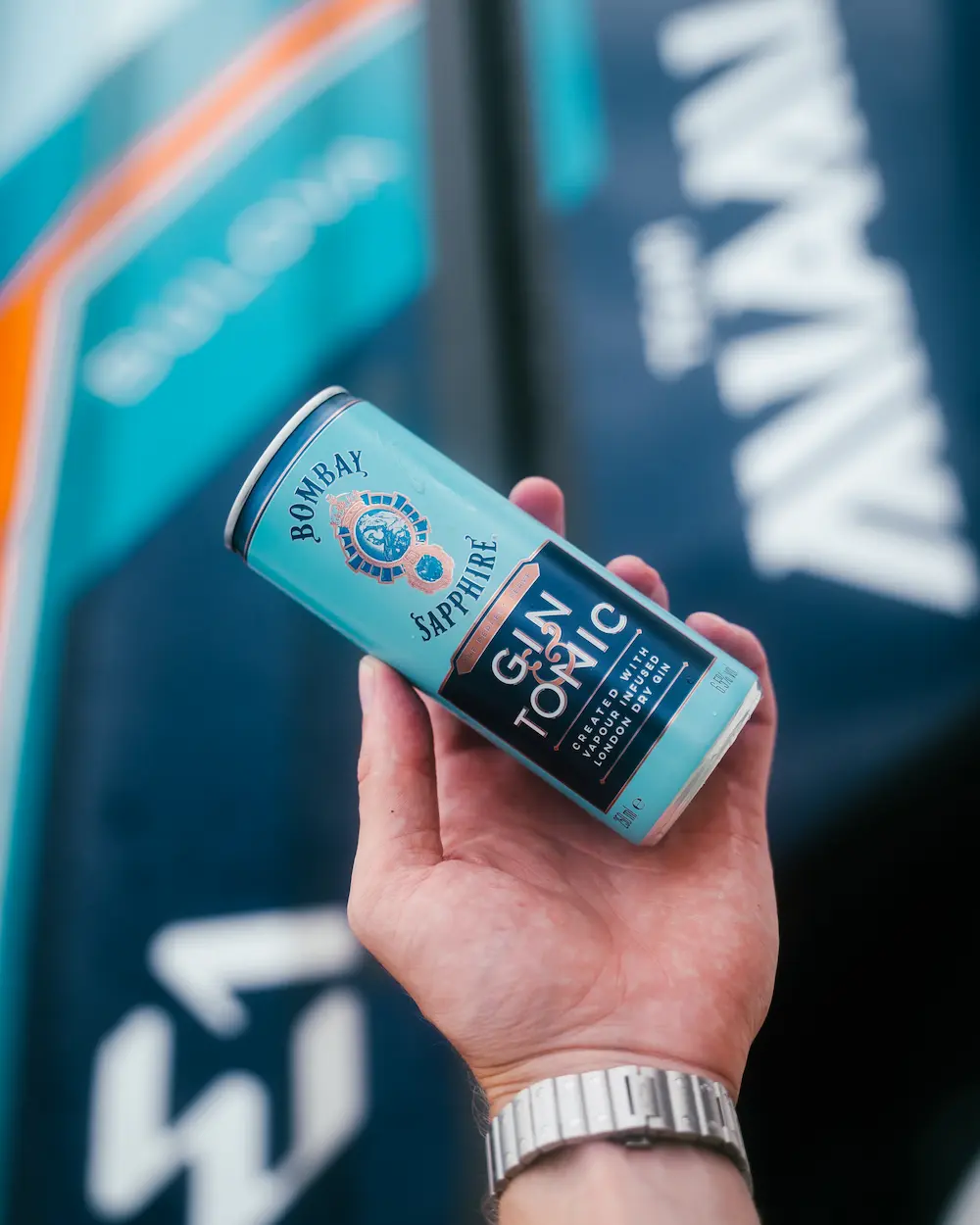 Branded Bombay Sapphire Gin & Tonic can held in front of the sleek turquoise and navy E1 Team Miami powerboat — showcasing the partnership between spirit and speed.