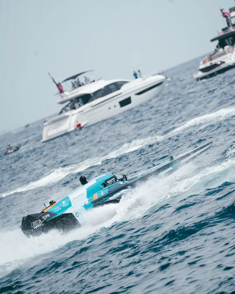 E1 Team Miami electric race boat cutting across Monaco waters during a competitive heat, with Azimut yachts and spectators in the background.