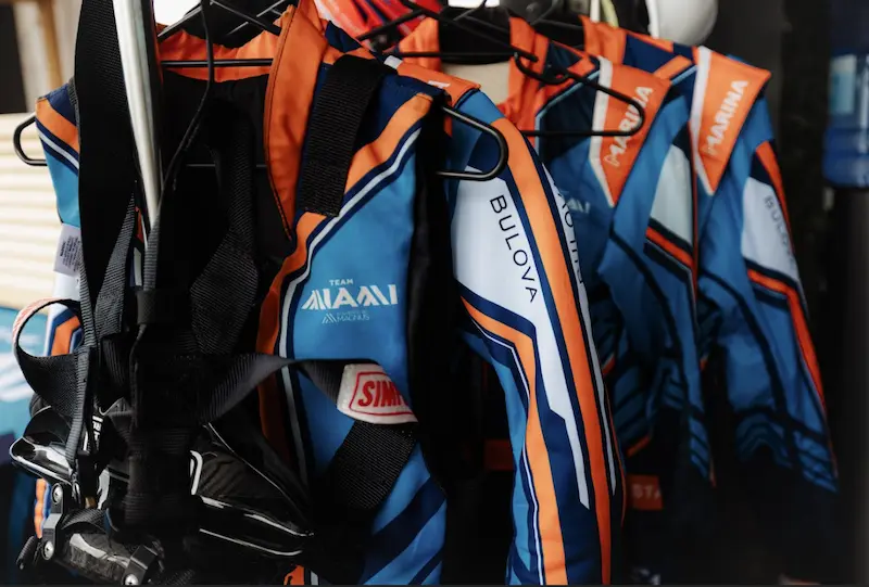 A lineup of E1 Team Miami racewear suits featuring bold blue and orange designs