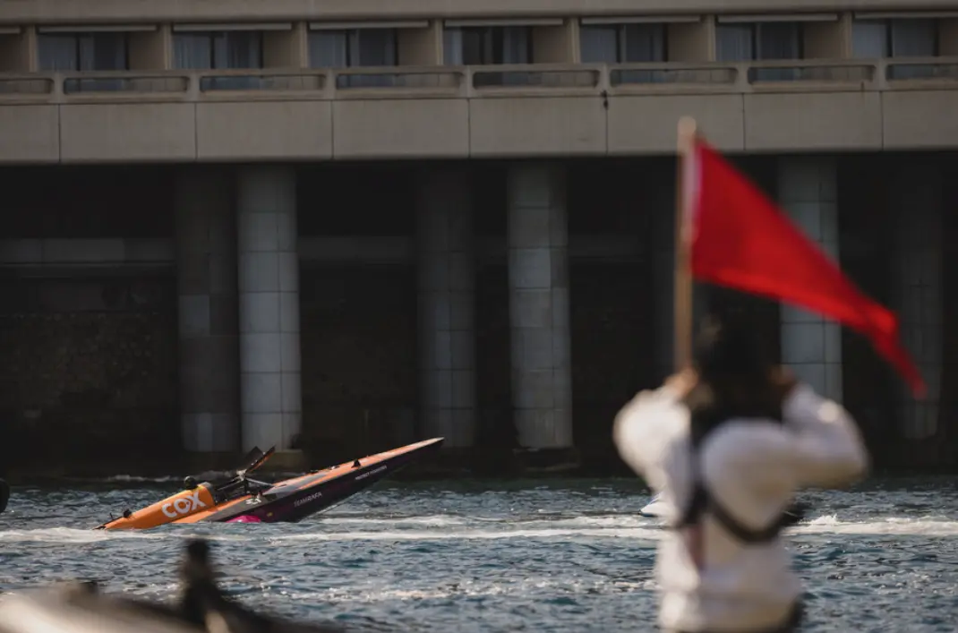 Team RAFA's electric raceboat slices through the water in front of a concrete bridge as a marshal raises a red flag in the foreground—capturing the intensity and precision of marine racing.