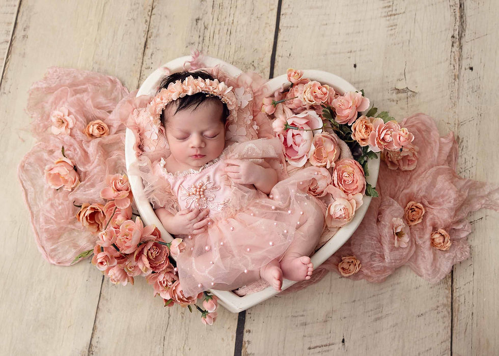 Sleeping newborn baby girl in pink lace dress in heart bowl surrounded by peach roses at Imagine That Photography Dix Hills Long Island