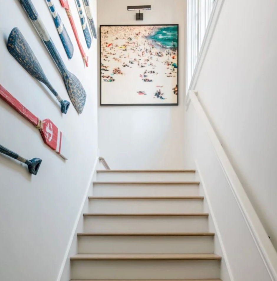 Bright white stairway with colorful oars on the left wall and a framed beach scene above the landing.