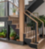Modern indoor staircase with wood steps, black railings, and potted green plants in a bright, airy home.