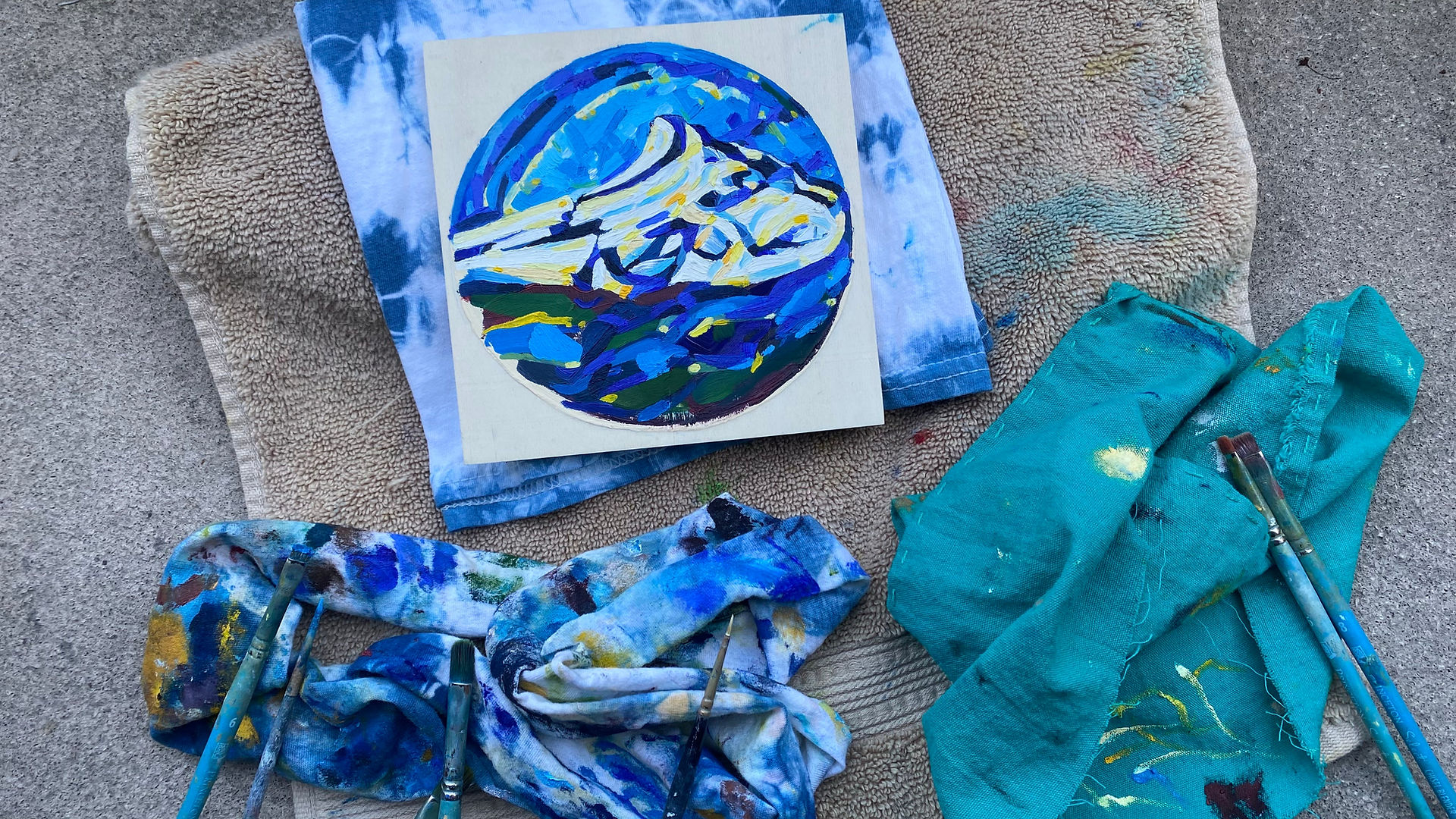 Art supplies: painting of blue mountains, on a red background with vibrant colors and paint brushes.