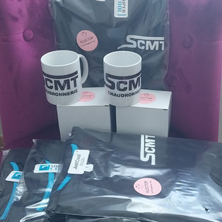 Ensemble de t-shirts et mugs personnalisés pour SCMT Chaudronnerie, avec logos imprimés et flex photochromique sur les textiles, exposés en lot.