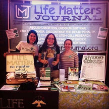 Aimee in 2014 standing at an expo table for Life Matters Journal