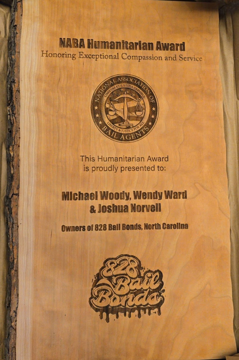 Wooden plaque for the NABA Humanitarian Award with engraved text and logo, honoring Michael Woody, Wendy Ward, & Joshua Norvell of 828 Bail Bonds.