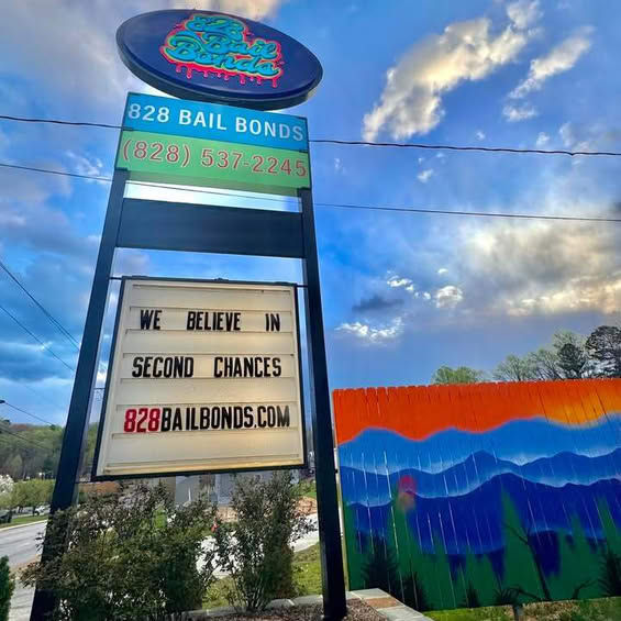 Tall 828 Bail Bonds sign reads We believe in second chances beside a colorful mural under a cloudy blue sky.
