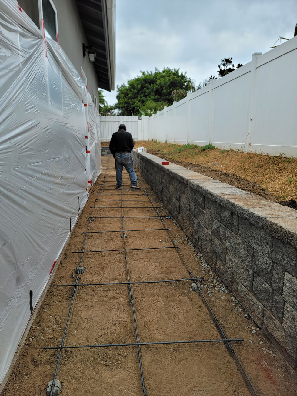 a man is working on a concrete walkway in front of a white fence