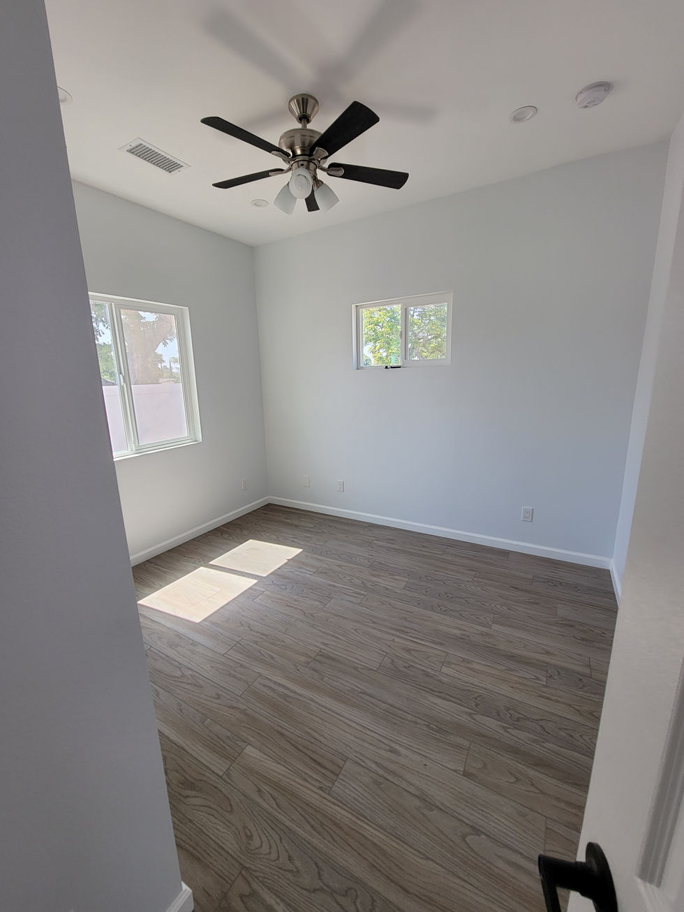 an empty room with a ceiling fan and two windows