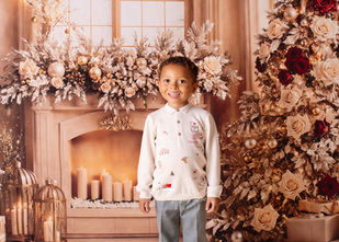 Little boy in festive outfit standing by a Christmas fireplace with warm lights and seasonal decorations — photographed at SA Photography studio in Eccles, near Salford, Worsley, and Monton, Greater Manchester.