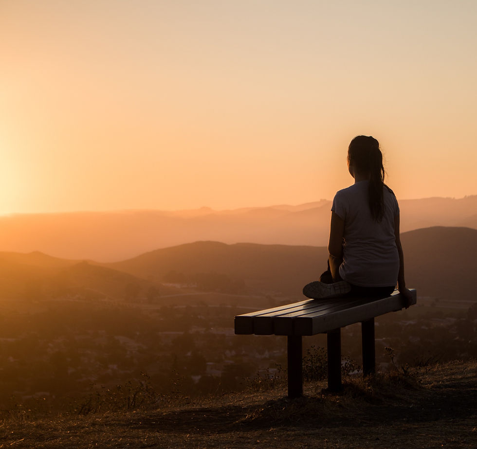Woman sits on a bench watching the sunset