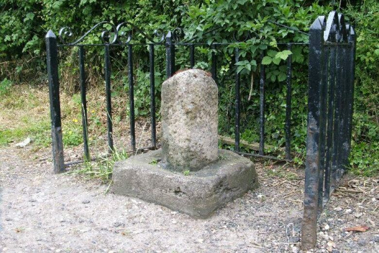 A sanctuary stone of Beverley sits in black, iron fencing. There are green bushes in the background.