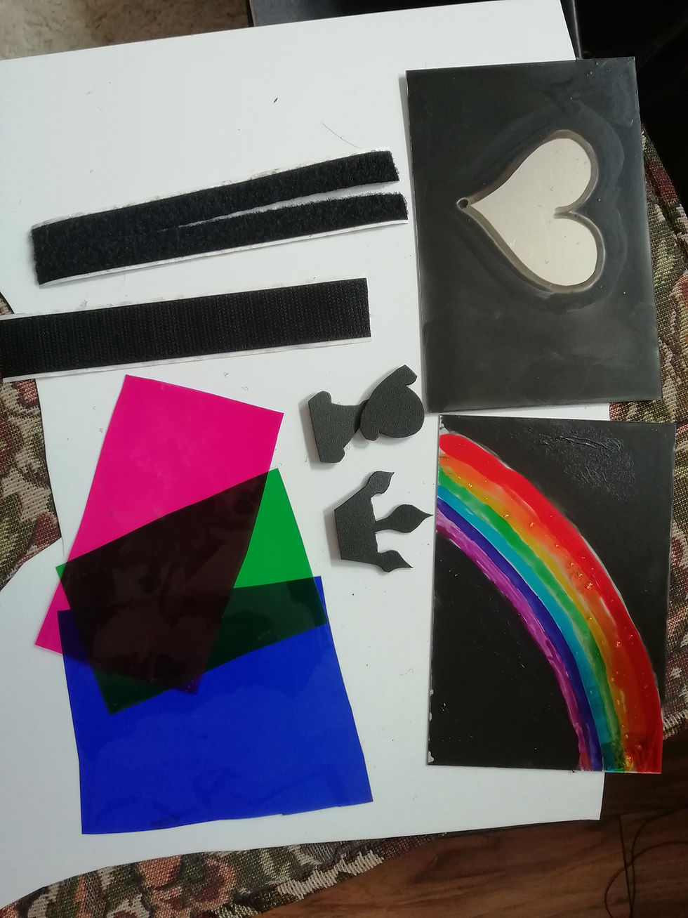 Some of the contents from the shadow kits are laid out on a table, including coloured acetate in pink, green and blue; a heart-shaped cut out and a painted rainbow.