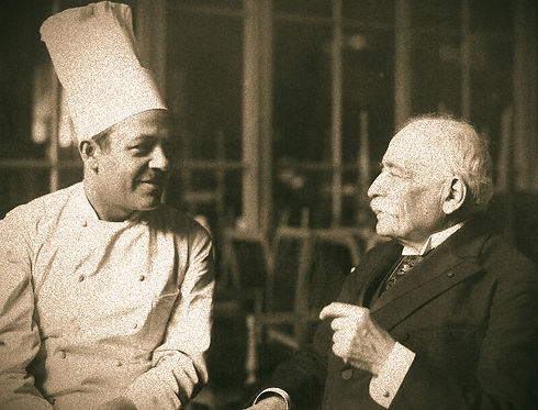 Escoffier-dressed-in-a-dark-suit-engages-in-a-friendly-discussion-with-a-chef-wearing-a-wh