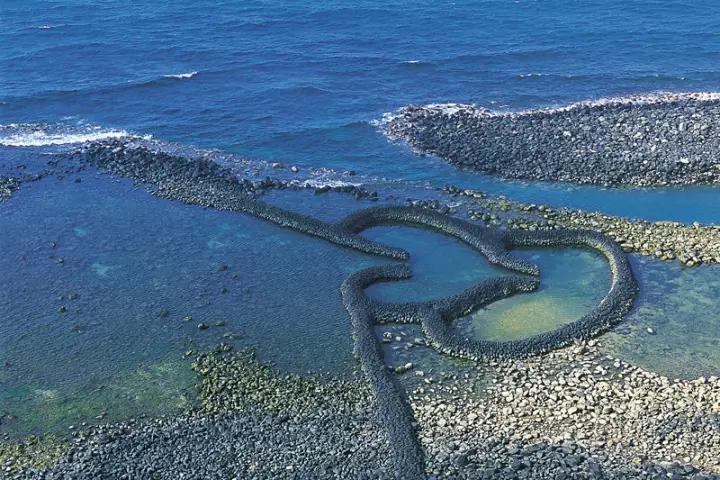 藍色海洋背景的雙心石滬，周圍是清澈見底的水和鵝卵石。整個畫面寧靜，充滿自然之美。