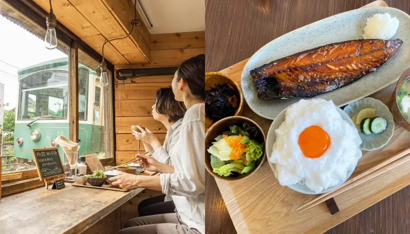 一對面朝窗外的顧客在木質內飾的餐廳用餐，窗外是一輛綠色電車。右側是烤魚、米飯和蔬菜的餐盤。